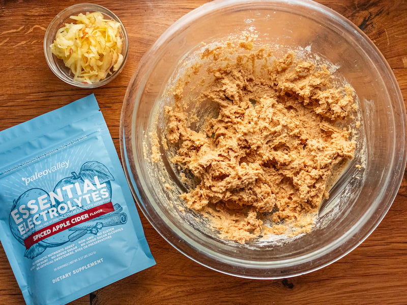 Bowl of cookie dough with shredded apples and PaleoValley Essential Electrolytes Spiced Apple Cider flavor on a wooden surface.