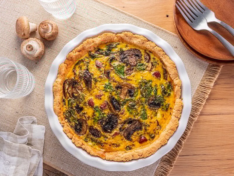 Savory quiche with mushrooms, kale, and beef jerky in a golden tallow crust, served in a white pie dish.