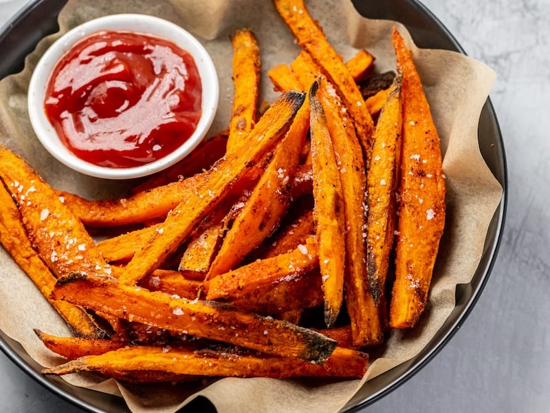 Crispy sweet potato fries cooked in tallow, sprinkled with sea salt, and served with ketchup in a parchment-lined black bowl.